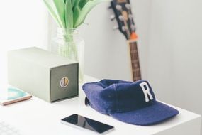 Blue and white cap and iphone lying on the office desk with the plant