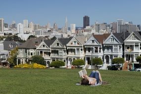 landscape of woman lying on the grass with a book and city