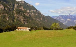 house on a green meadow near the mountain, italy, prato