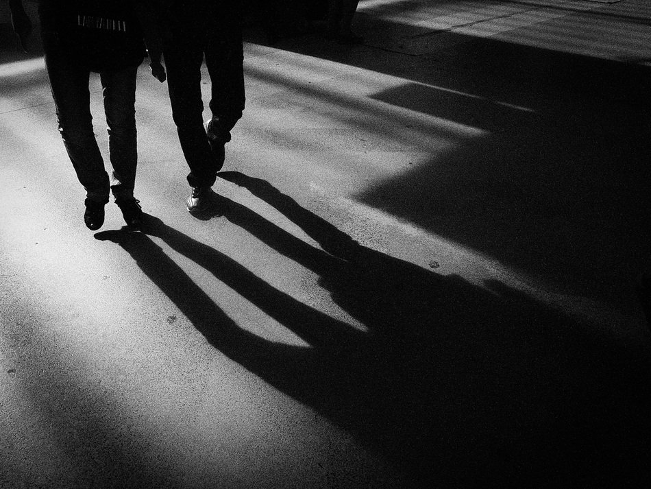 monochrome picture of people walk along the road near the shadow