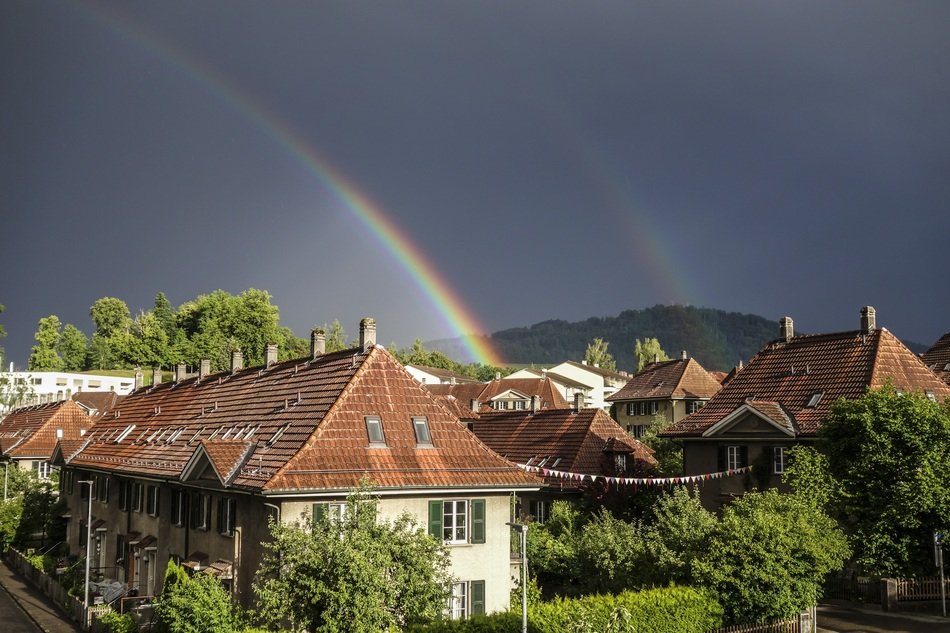 Colorful and beautiful rainbow over a village among the plants in Switzerland