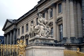 VersStatue of sitting woman with caduceus at golden fence of palace, france, versailles