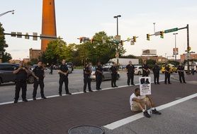 Black Lives Matter, policemen staying at sitting on street man with Protest Sign