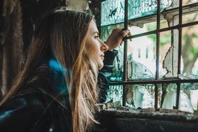 girl looking through the broken window glass