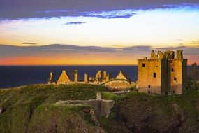 dunnottar castle on a green hill during sunset, scotland