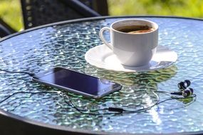 cup of coffee, headphones and a smartphone on a table in an outdoor cafe