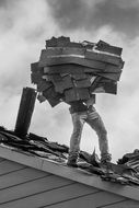 Workman holding old tiles on roof