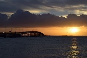 silhouette of long Bridge above calm glossy water at sunset