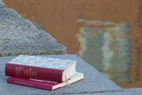 two closed books on stone wall at water
