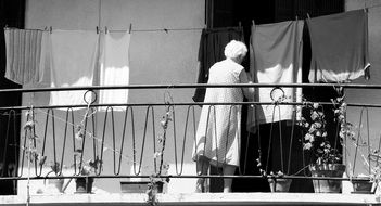 elderly woman hangs clothes on the balcony