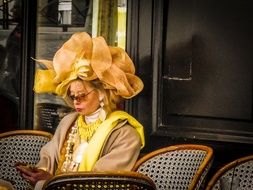 portrait of woman in designer hat sits on a chair in France