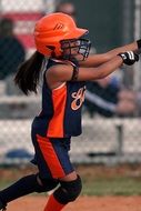 girl in uniform and orange helmet plays softball