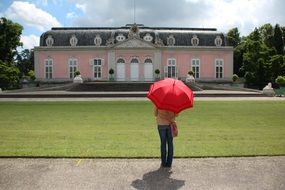 man with a red umbrella stands near the castle