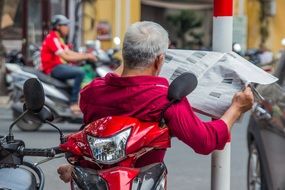 man on a scooter reading a newspaper