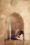 girl plays traditional jewish Music in niche of ancient stone wall, israel, Jerusalem