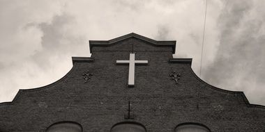 Black and white photo of the building with a large cross on the facade at cloudy sky background