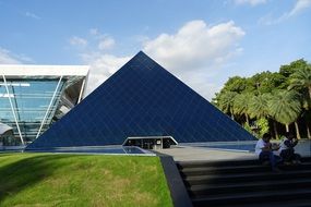 people sit on the stairs on the background of a glass pyramid near the plants in Karnataka, India