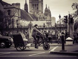 Black and white photo of a cyclist in city traffic at background with the buildings