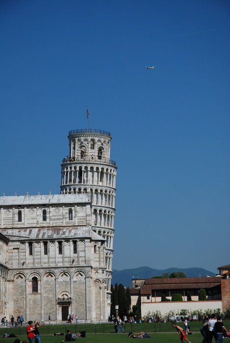 leaning tower behind a building in pisa under a blue sky