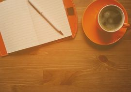 orange cup of coffee and orange notebook