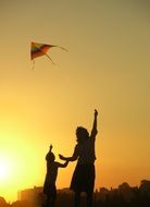 mother with a child fly a kite on a sunset background