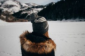 girl in a hat at the winter lake at the foot of the mountain