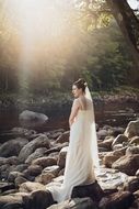 girl in a wedding dress on a rocky bank of a river