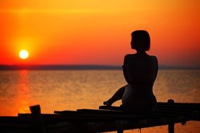lonely girl on the pier against the backdrop of a fiery sunset