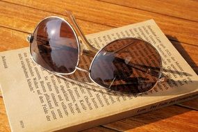 Sunglasses at top of book on wooden surface