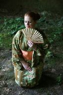 Japanese girl with a fan sits on the ground