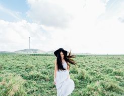 happy Young Woman in black hat walks on meadow