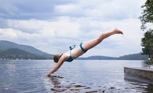 woman in bikini is jumping into the river