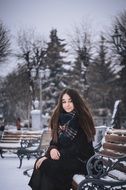 girl in a black coat sits on a bench in winter