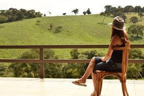 Woman sits on Chair in view of Green hill
