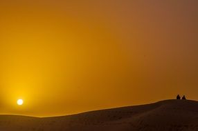 people on a hill in the desert against the backdrop of a golden sunset