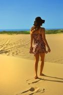 Woman wearing black hat and colorful dress walks on Sand Beach