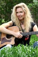 girl with a guitar sits on green grass
