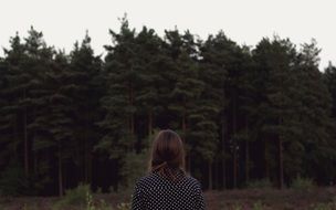 girl stands facing a dense forest