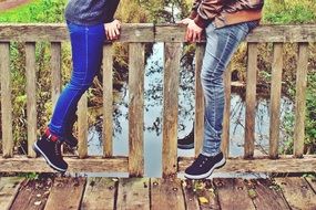 legs of a couple in love on the railing of a wooden bridge