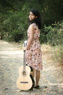 young Girl with guitar stands on road at forest