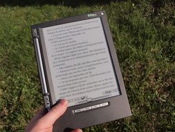 e-reader in female hand at lawn