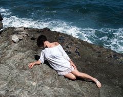 girl in a white dress lying on a rock by the sea