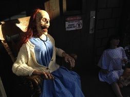 dead woman sits in armchair, mannequin