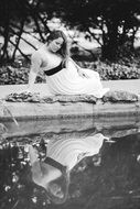 photo of a pregnant girl in a white dress on the shore of the pond