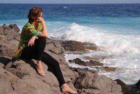 pensive woman sitting on stones at the beach