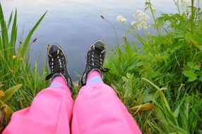 female Legs in pink pants and sneakers on grass at water