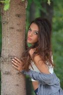 young caucasian girl posing at tree trunk