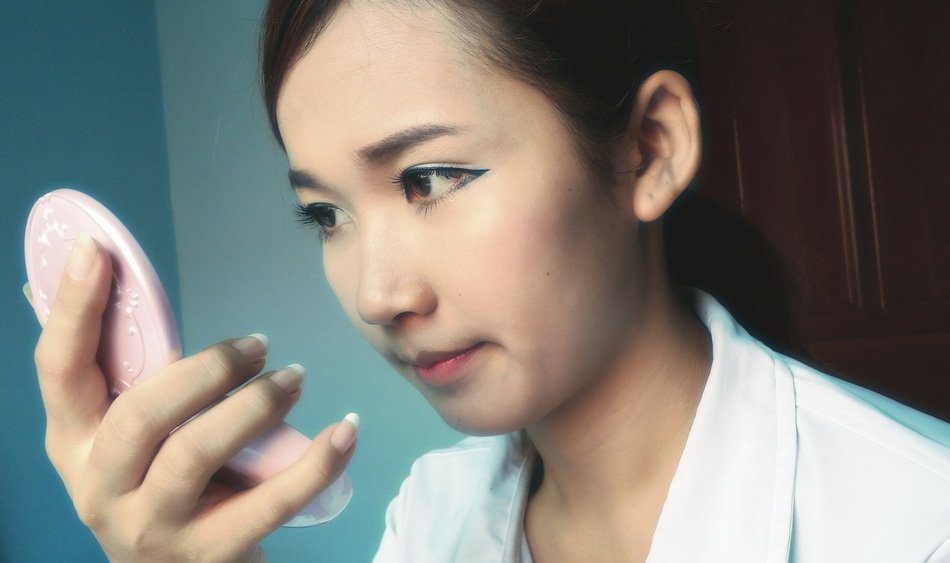 young asian with make up looking in the mirror