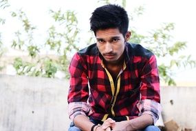 Serious man in red shirt sits outdoor