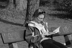 black and white photo of a woman with a book on a bench